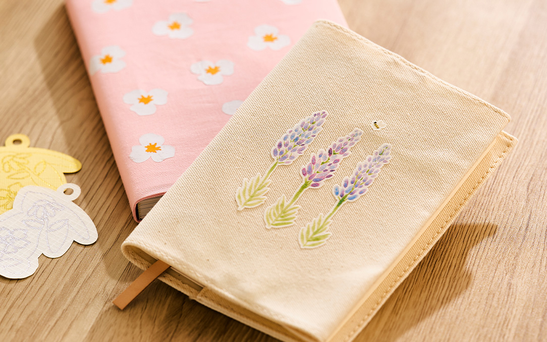 Close-up of a canvas journal cover decorated with lavender heat transfer vinyl and surrounded by other floral-themed crafts