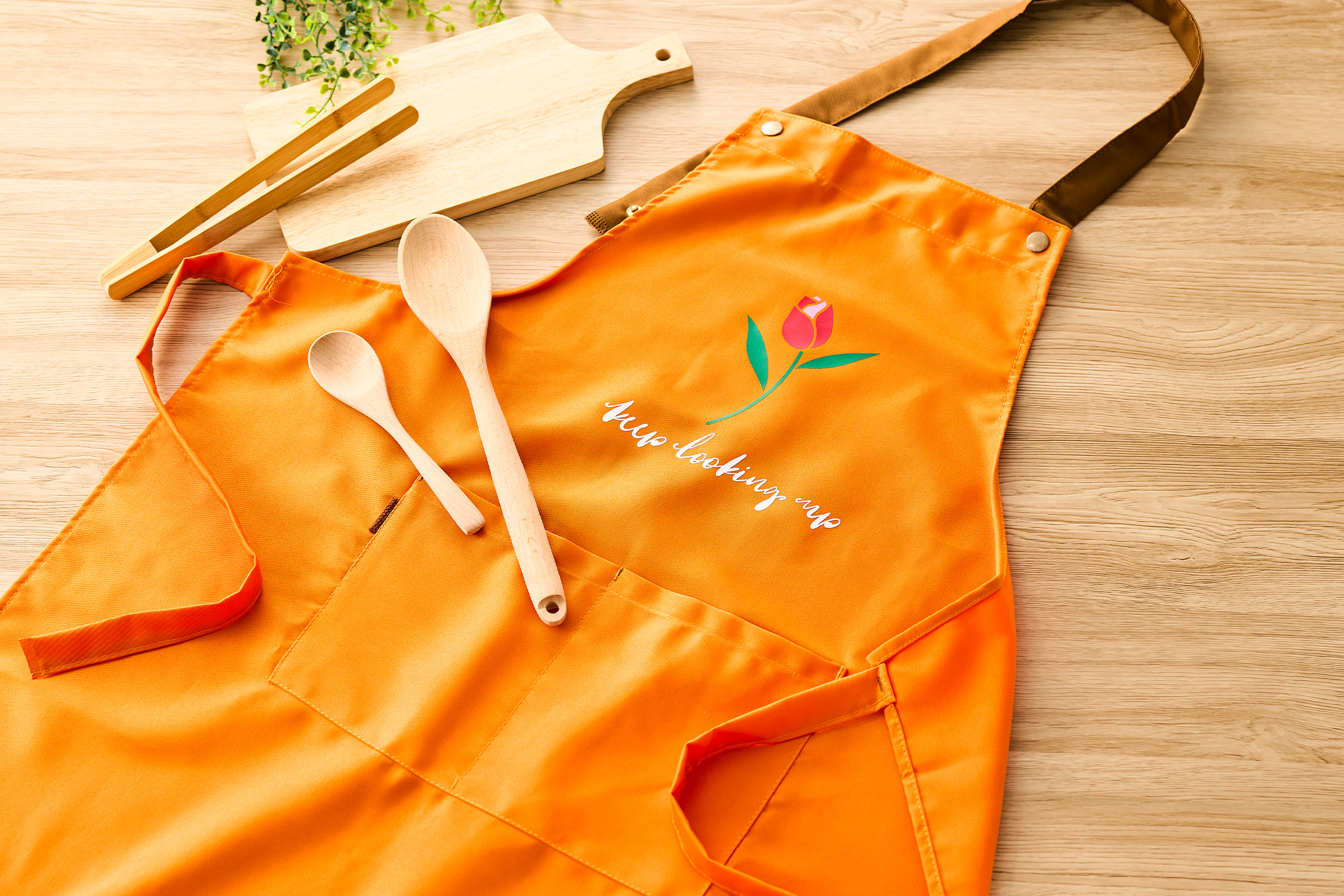 Customized orange apron with “Keep looking up” vinyl design and tulip graphic, displayed with wooden spoons and cutting boards