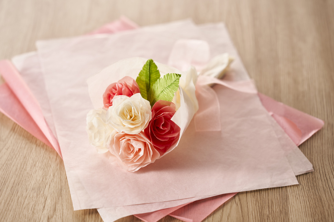 Close-up of pink paper flowers with green leaves in white vases