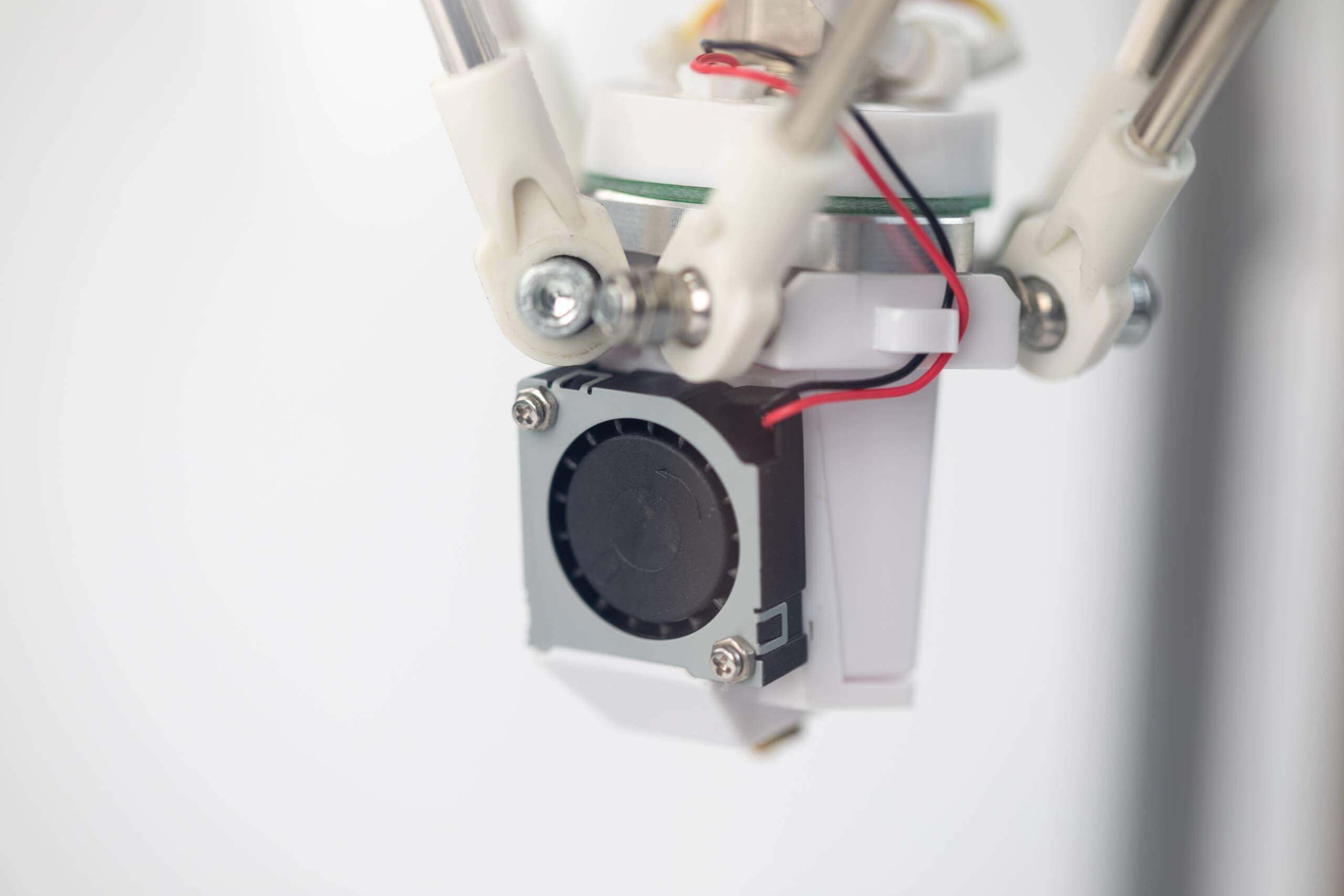 Close-up of the fan and mechanical components of a 3D printer, showing wires, bolts, and structural elements of the printer's extruder assembly.