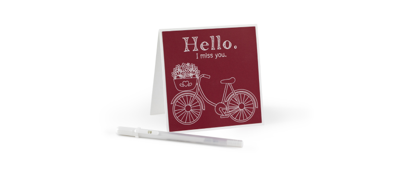 Greeting card with a red background and white illustration of a bicycle and the text 'Hello. I miss you.' next to a white pen.
