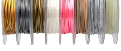 Spools of specialty 3D printer filament in various colors and finishes, including gold, silver, white, pink, bronze, and metallic hues, arranged side by side.